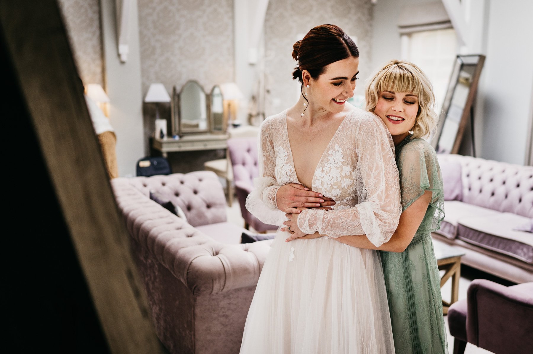 A bridesmaid hugs the bride from behind whilst getting ready during bridal prep