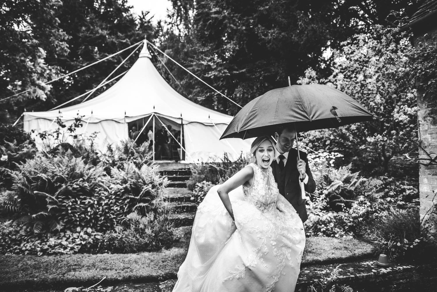 groom holds umbrella for bride during oxford garden wedding with tent