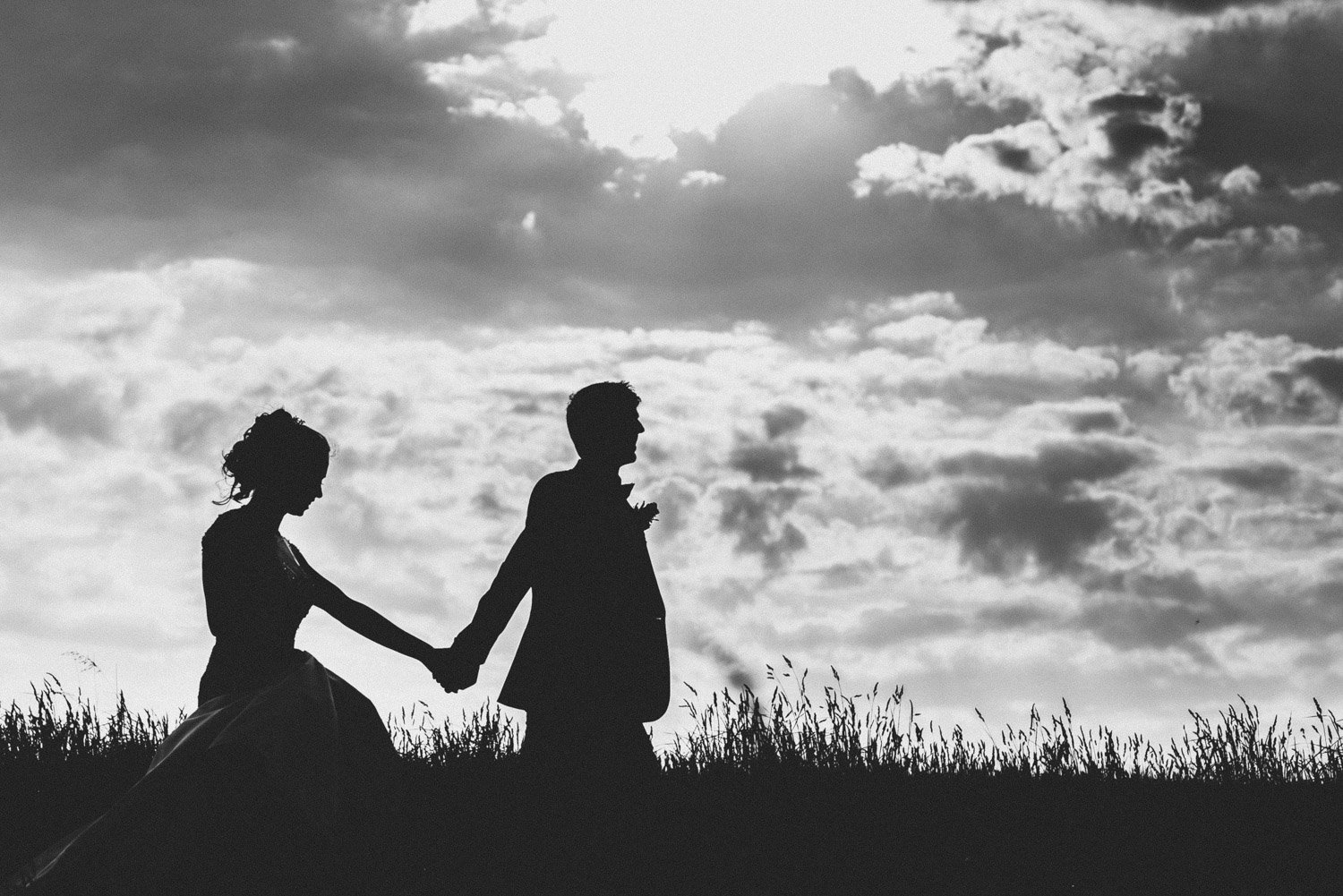 silhouette of couple holding hands in field at stone barn, cheltenham