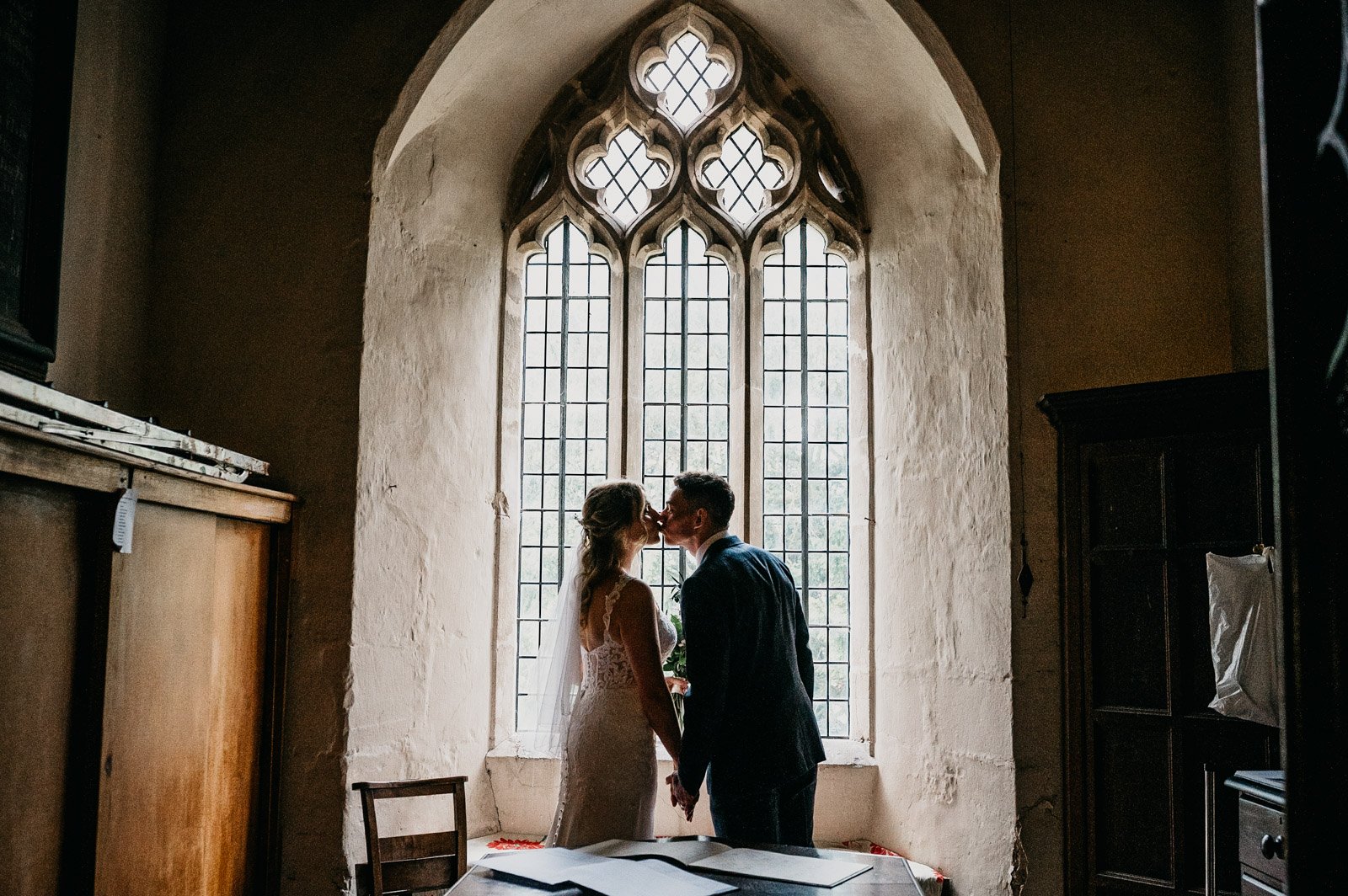 newlyweds kiss in front of church window 