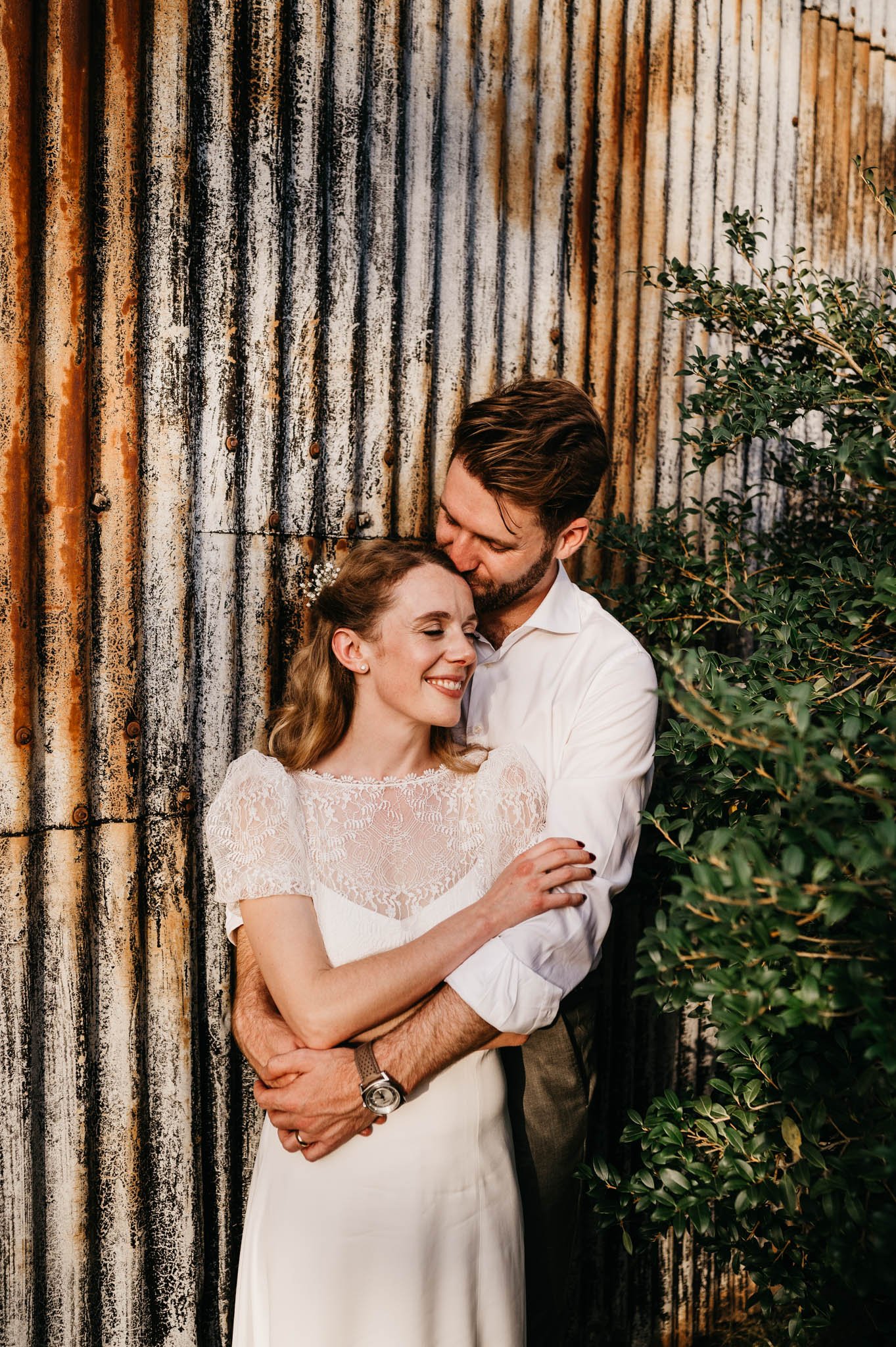 bride and groom cuddle in front of rustic barn at cripps stone barn wedding venue