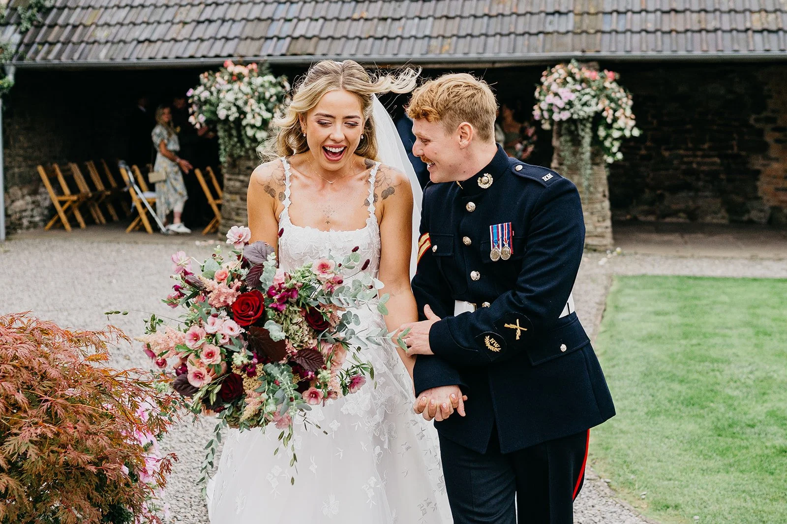 Groom in military uniform and his bride with floral red bouquet