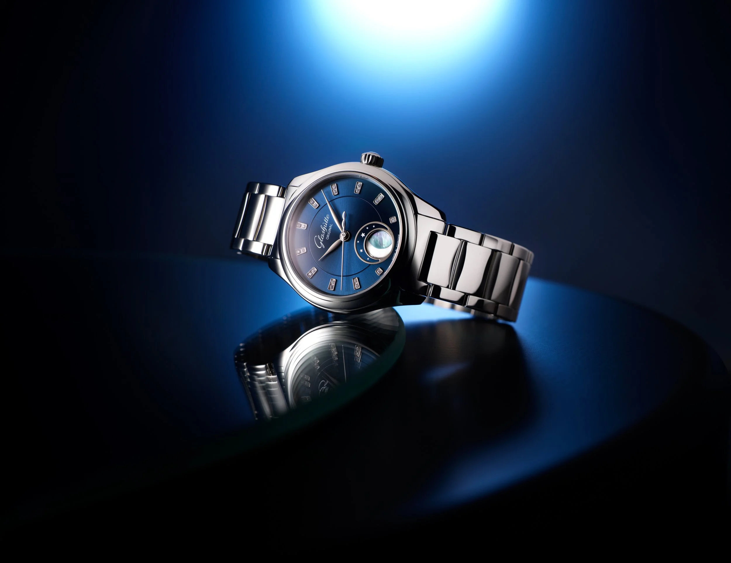 Photo de pub pour lancement montre Glashütte: Montre élégante en métal avec un cadran bleu, reflet sur une surface noire, éclairage dramatique
