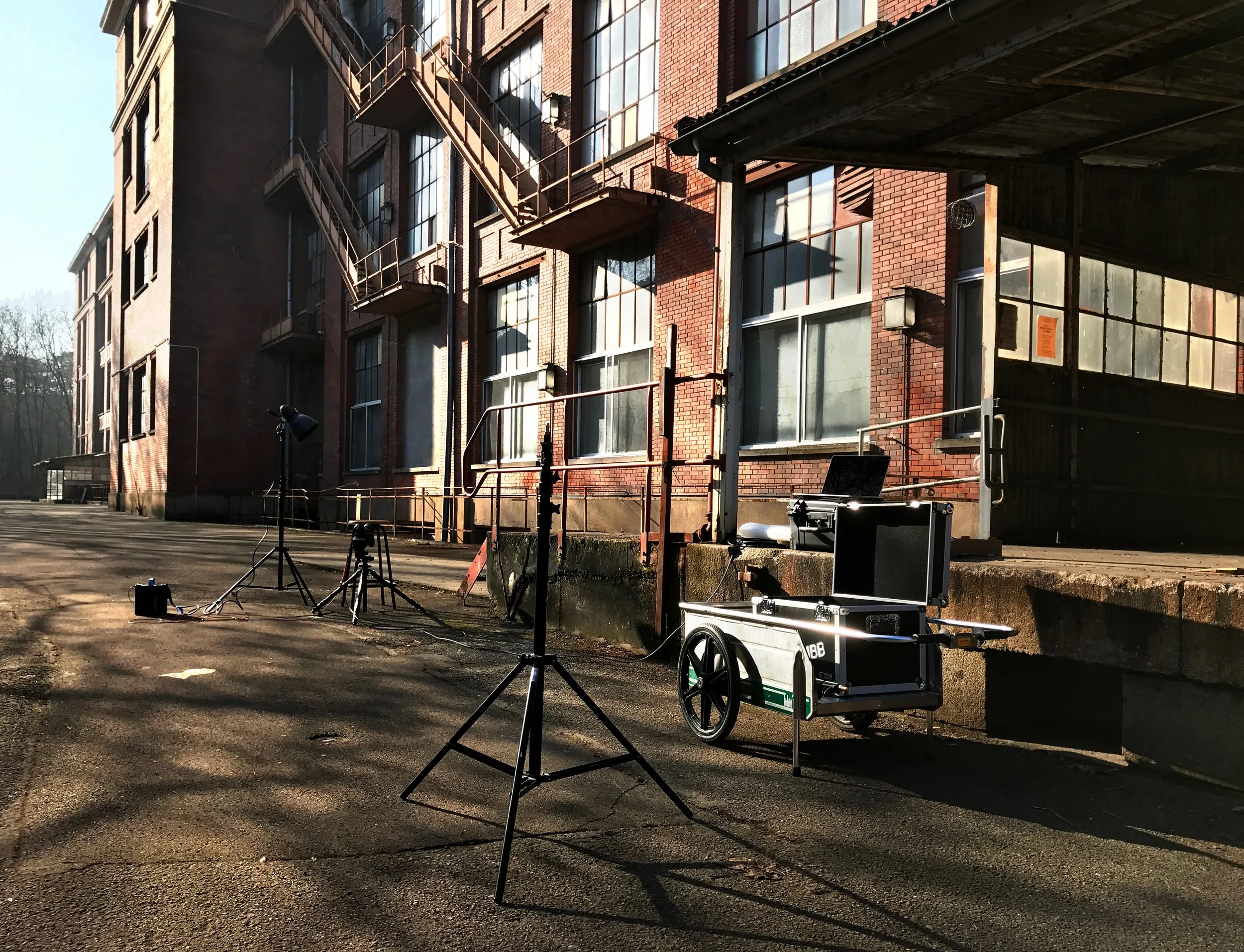 Making off shooting pro de montre: Équipement de prise de vue ou de photographie installé devant un bâtiment en briques, comprenant des trépieds, des lumières.