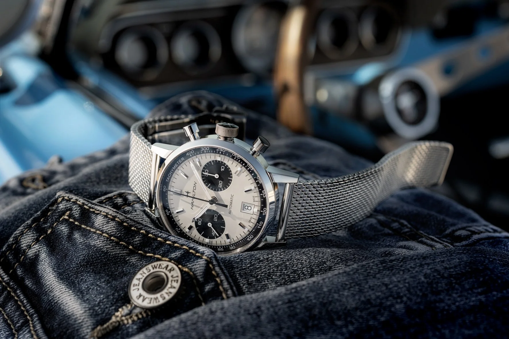 Photo publicitaire pour Hamilton: Une montre posée sur une poche de jean, avec l'intérieur d'une voiture en arrière-plan.