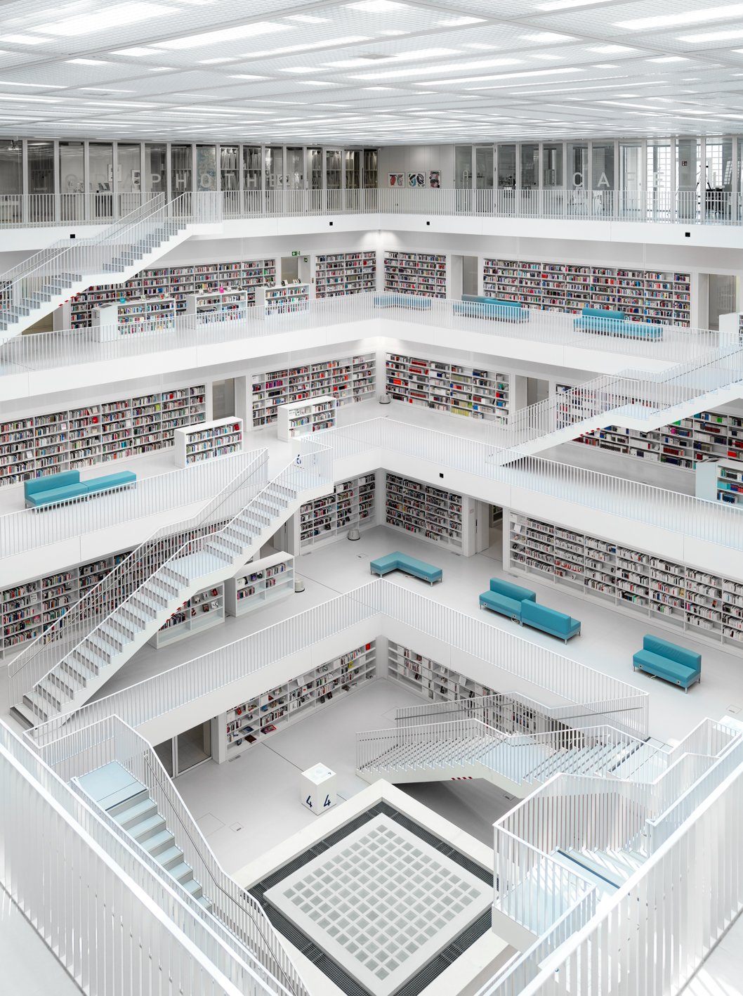 Photographie d'architecture: Bibliothèque moderne à plusieurs étages avec des étagères remplies de livres, des escaliers en blanc et des canapés bleus.