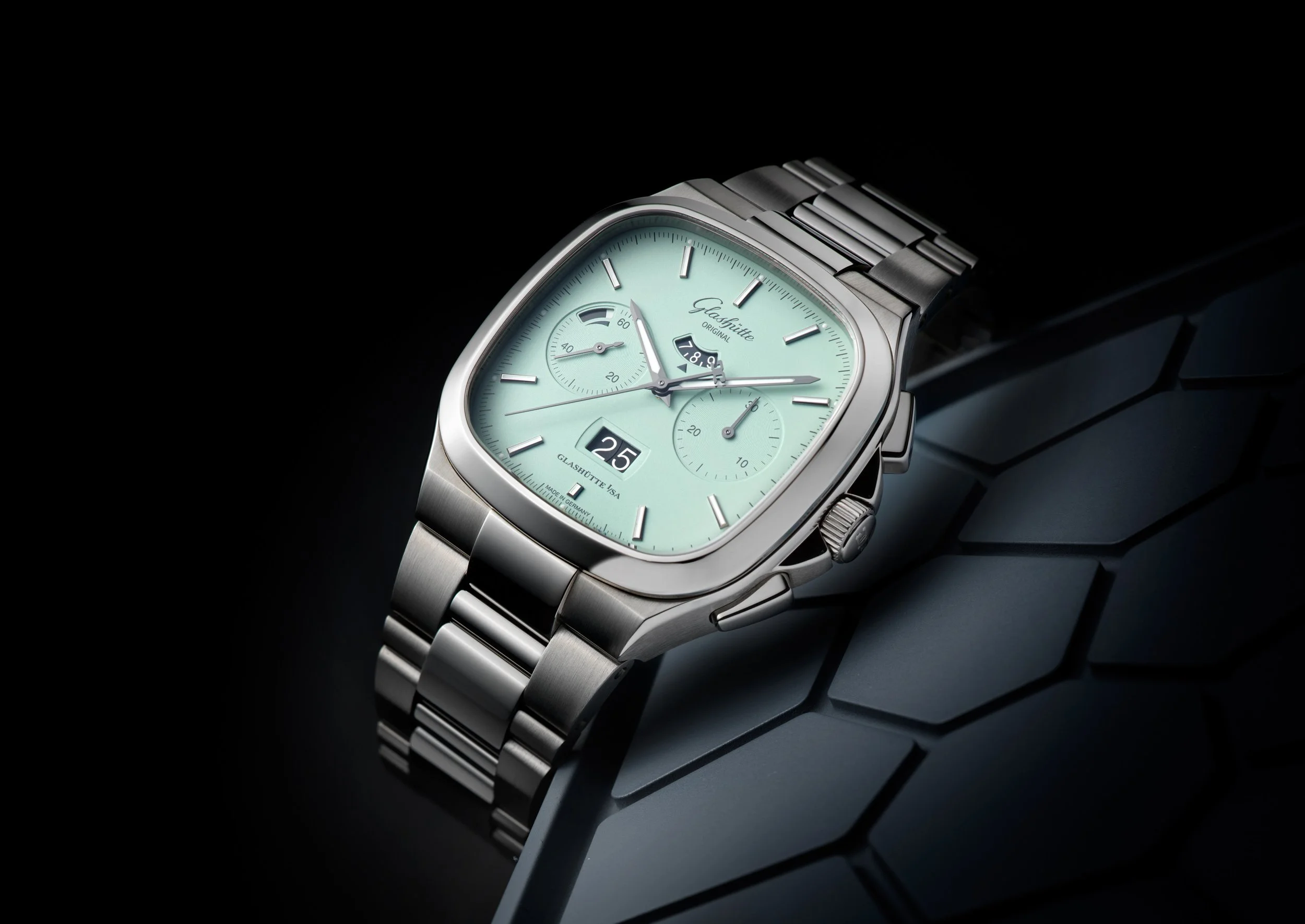 Photo de pub pour lancement montre Glashütte: Montre en acier avec cadran vert pâle, chronographe, affichage de la date, et bracelet métallique, posée sur une surface noire