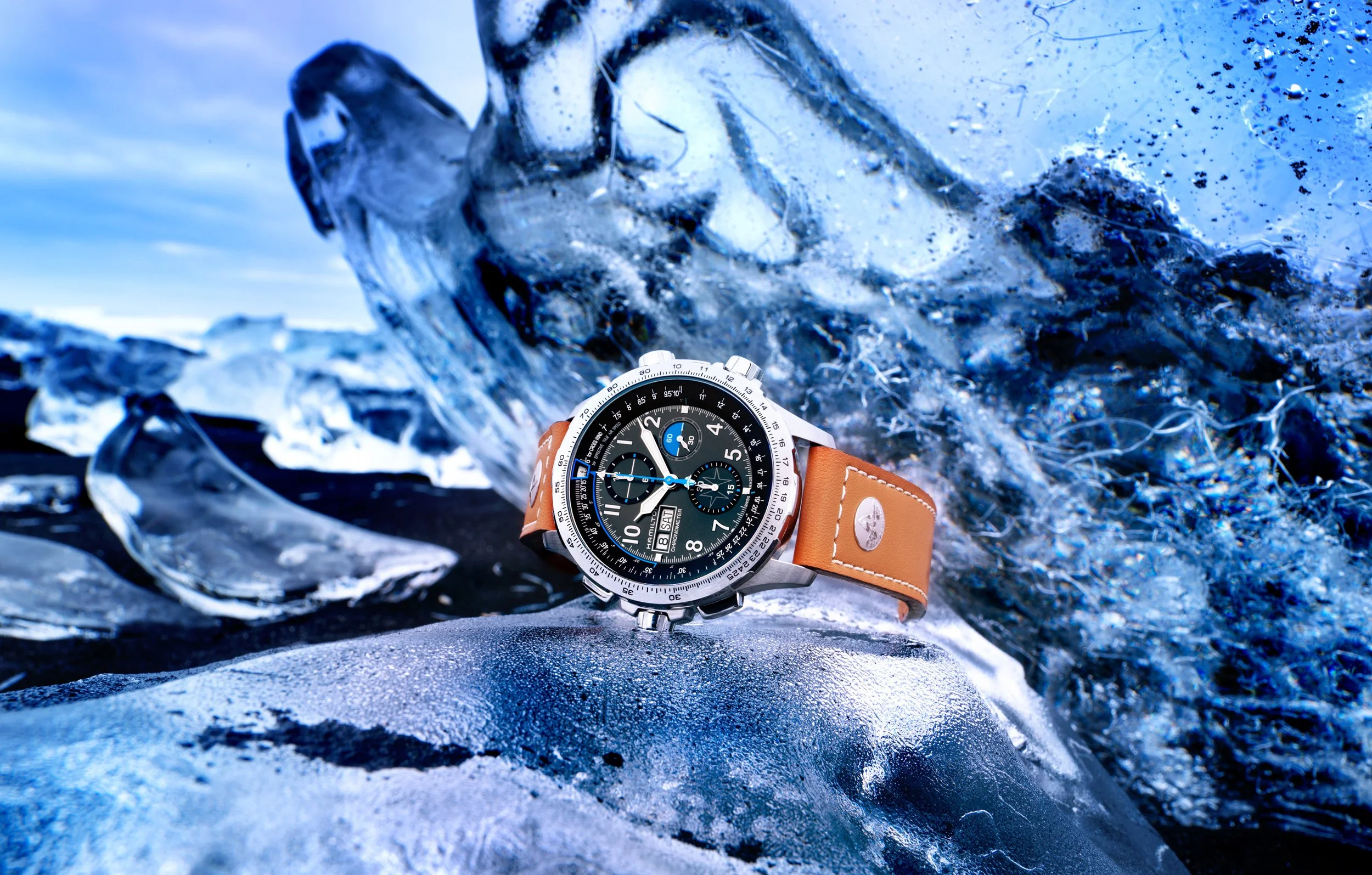 Photo publicitaire pour Hamilton: Montre de luxe avec un bracelet en cuir marron posée sur de la glace bleue, avec des blocs de glace en arrière-plan.