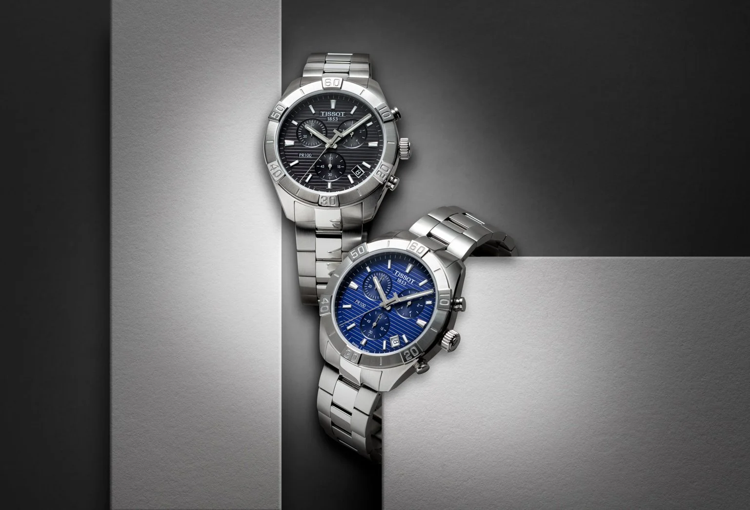 Visuel pub pour Tissot: Deux montres en acier inoxydable avec cadrans noirs et bleus, disposées sur un fond en nuances de gris