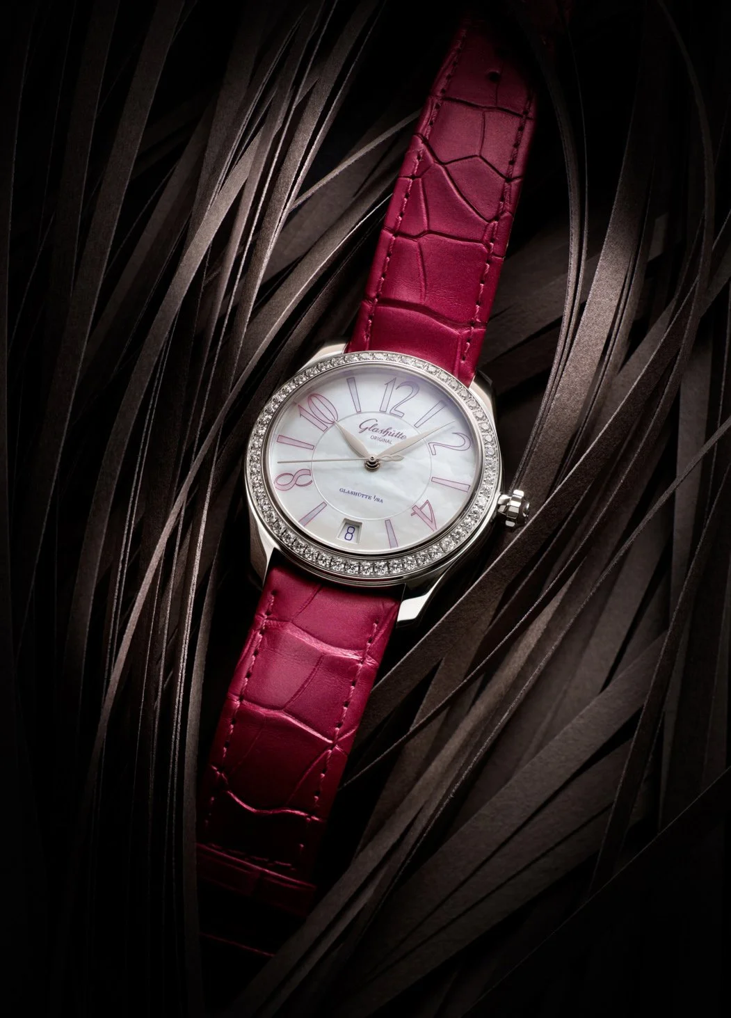 Photo de pub pour lancement montre Glashütte: Montre de luxe avec un cadran blanc, chiffres arabes roses et un bracelet en cuir rouge crocodile, entourée de diamants.