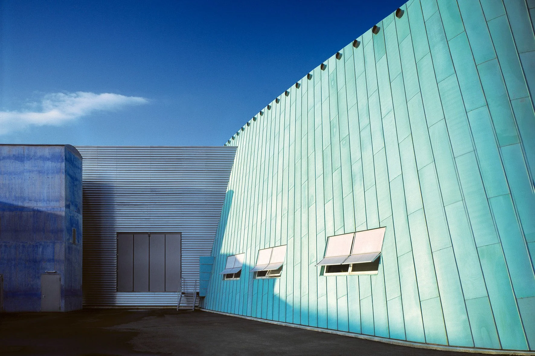 Photographie d'architecture: Bâtiment moderne en acier avec plusieurs fenêtres orientées vers le haut, ciel bleu clair en arrière-plan.