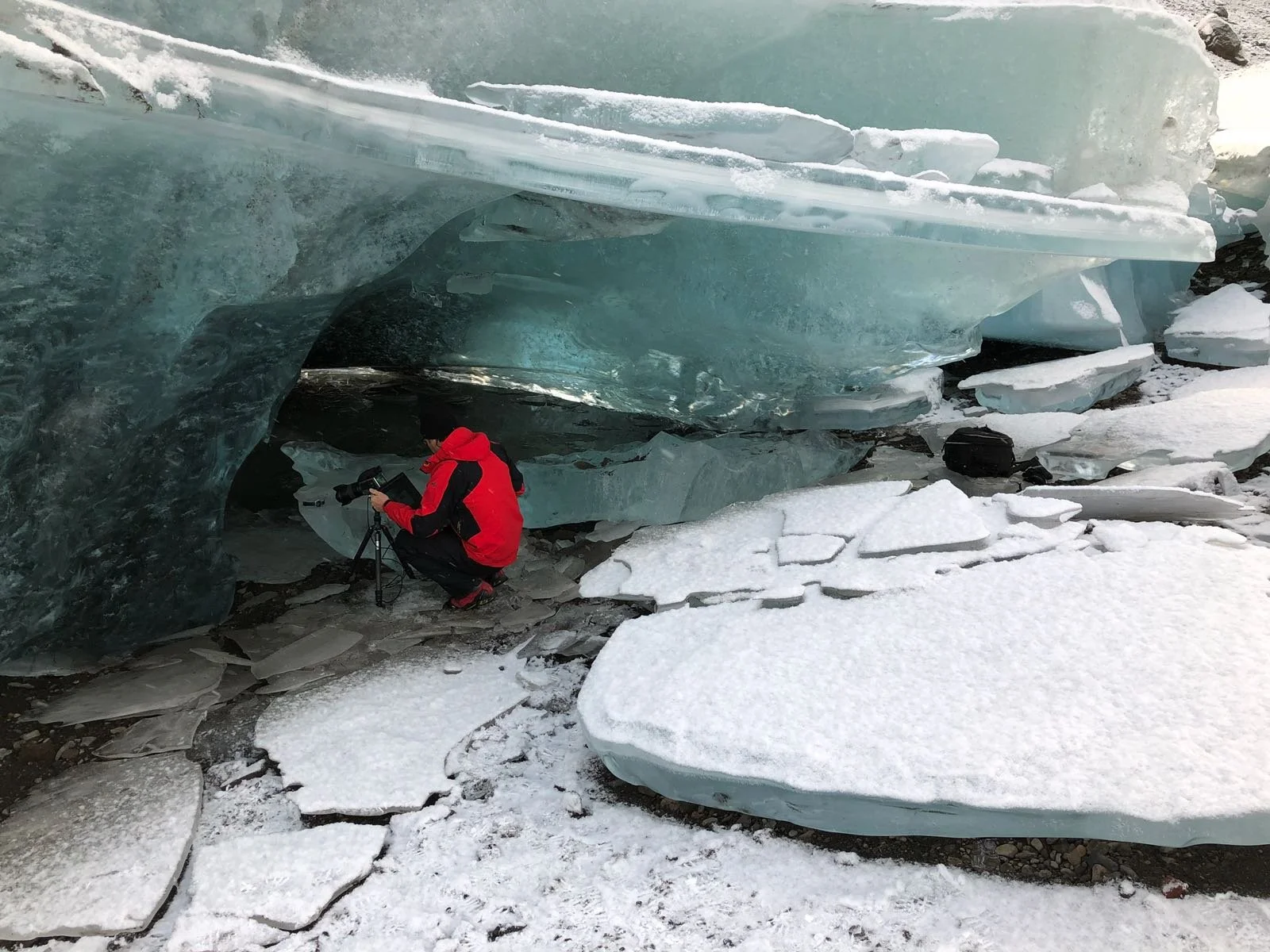 Making off shooting pro de montre: Un photographe prend une photo sous un grand bloc de glace dans un paysage enneigé.