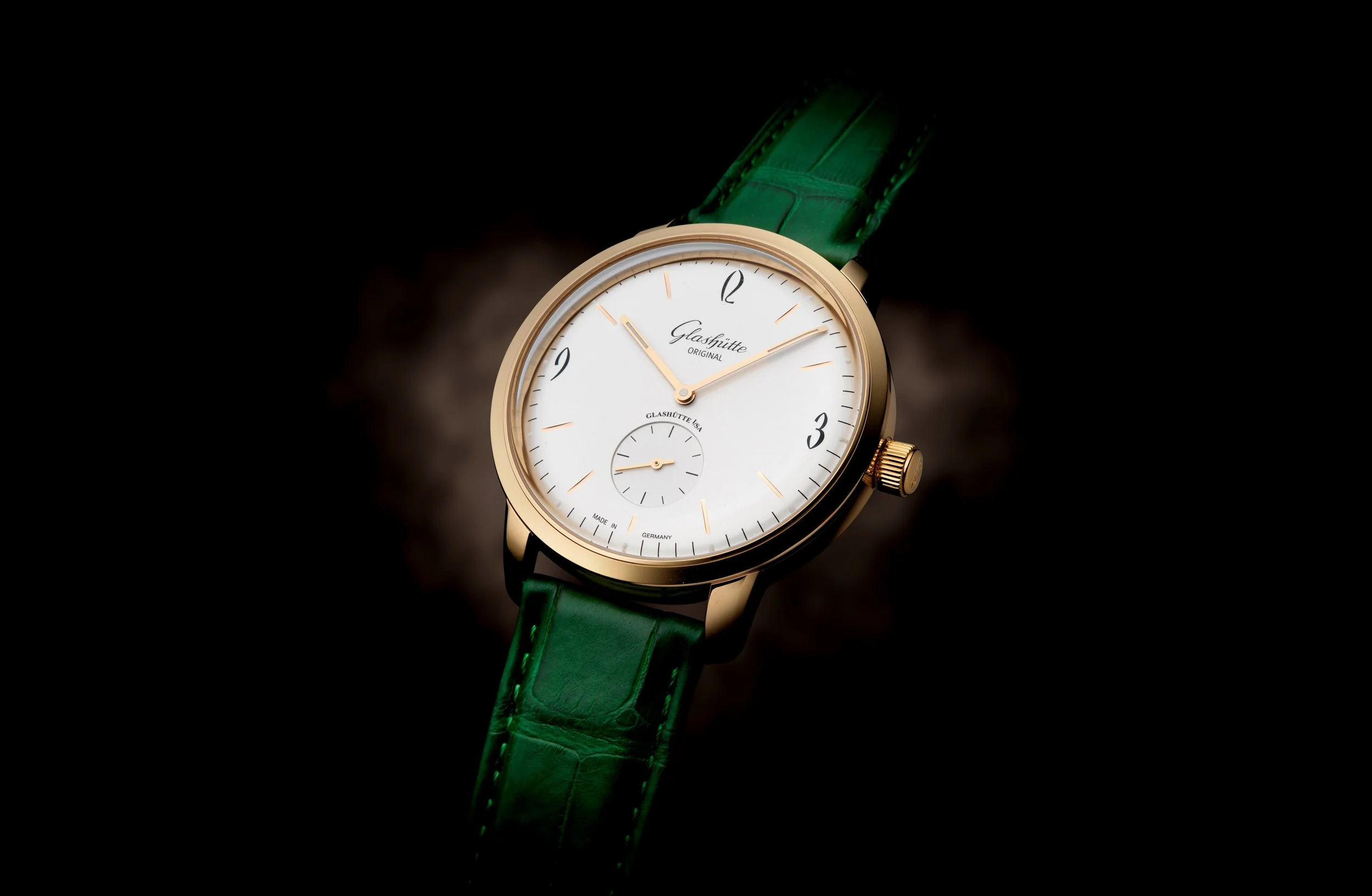 Visuel pub pour Glashütte: Montre avec un cadran blanc, boîtier en or et bracelet en cuir vert.