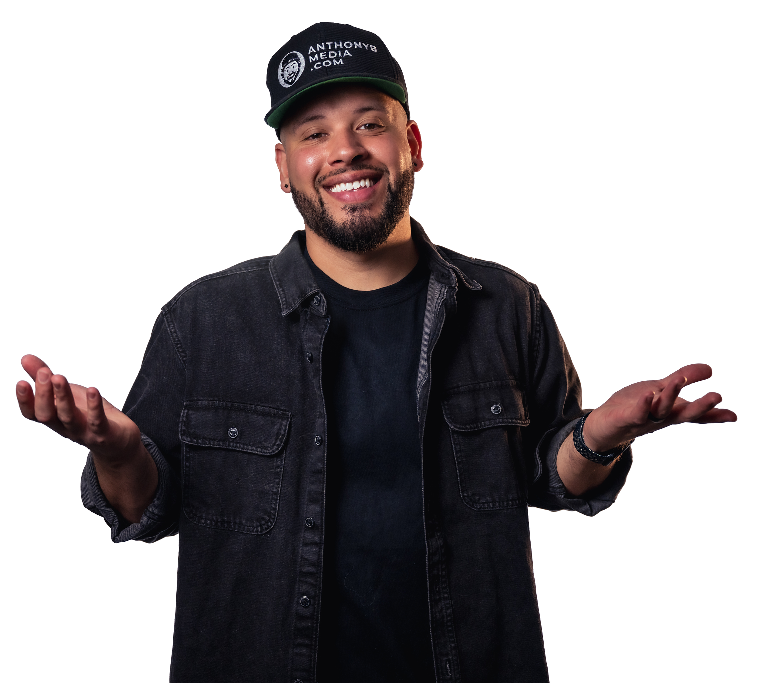 A man with a beard and mustache wearing a black cap that says ANTHONYB MEDIA and a black denim shirt, smiling and shrugging his shoulders.