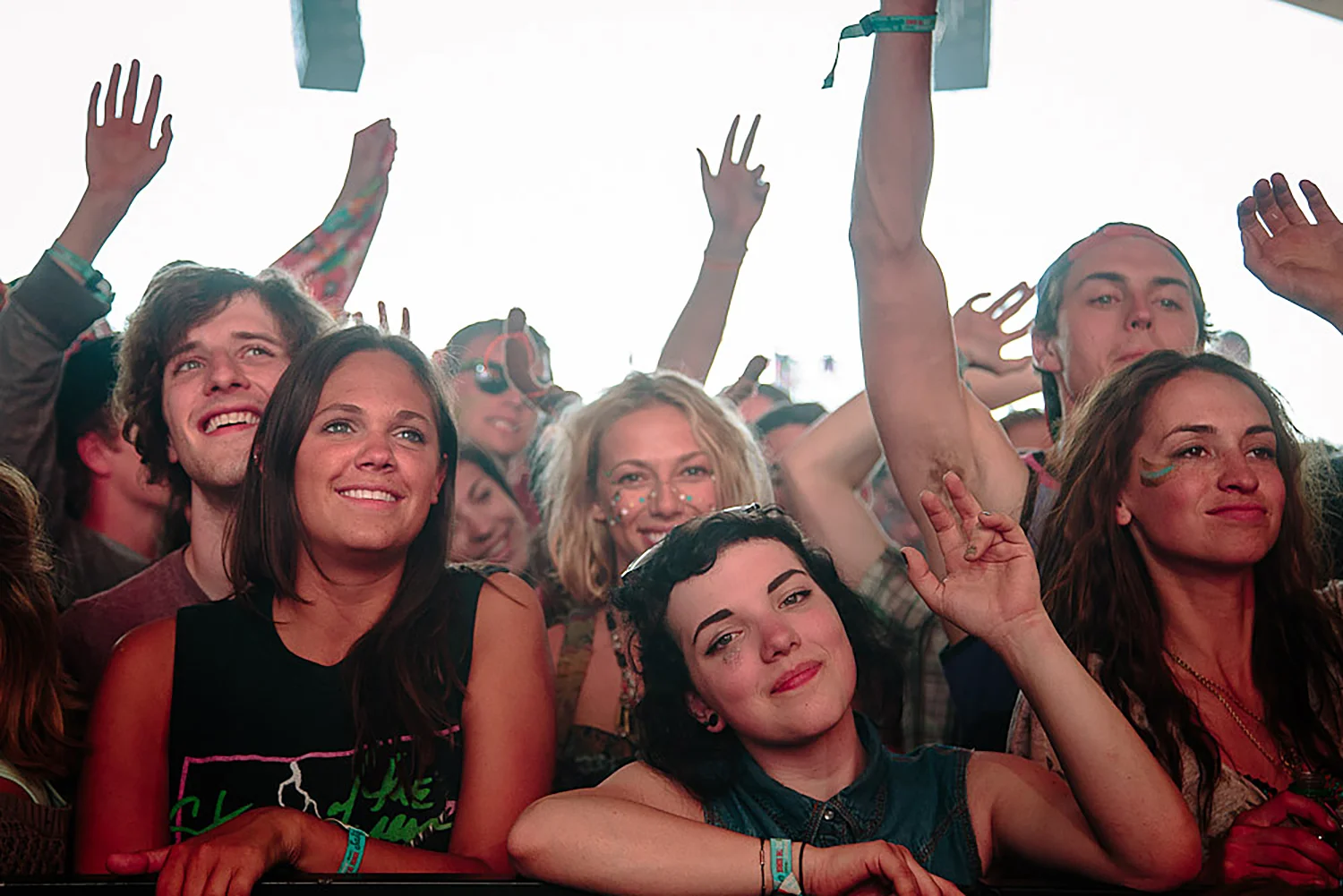 Crowd of young people at a concert, some raising their hands and smiling