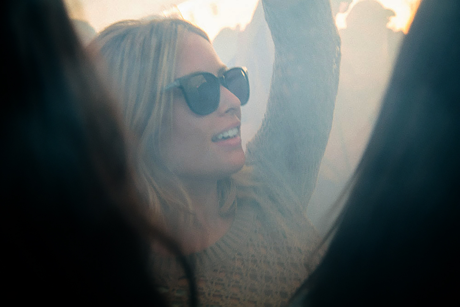 A woman on a boat, smiling and wearing sunglasses, with her arm raised, enjoying a sunny day.