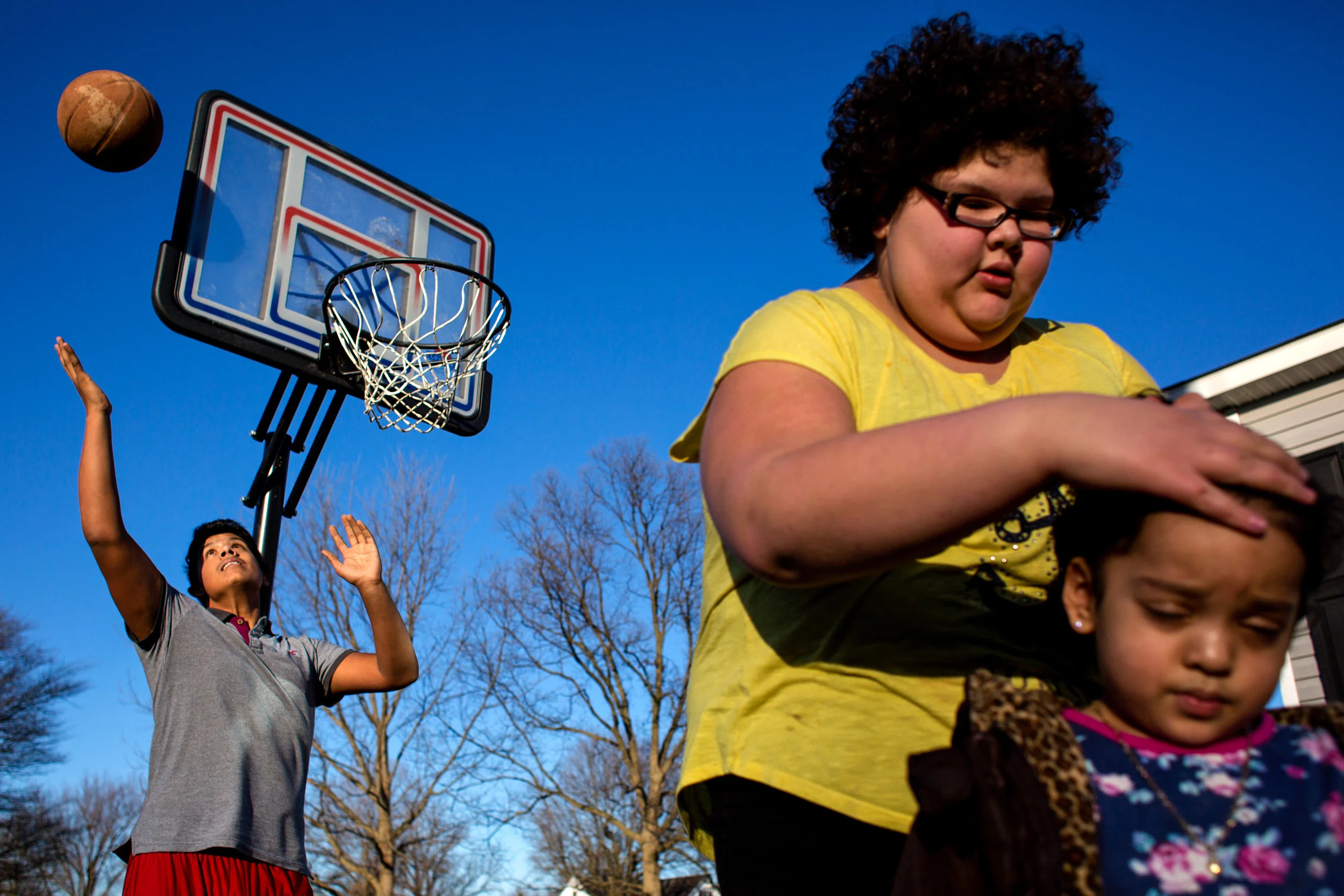 Melvin Orellana, 15, left, caught a rebound while his sister Margery Villalta, 11, tied up the hair of their cousin Cinita Lopez, 3, all of Huntingburg, on Wednesday afternoon outside their home in Huntingburg. The cousins took advantage of this week’s unseasonably warm weather — Wednesday’s highs reached into the 60s — and played outside.