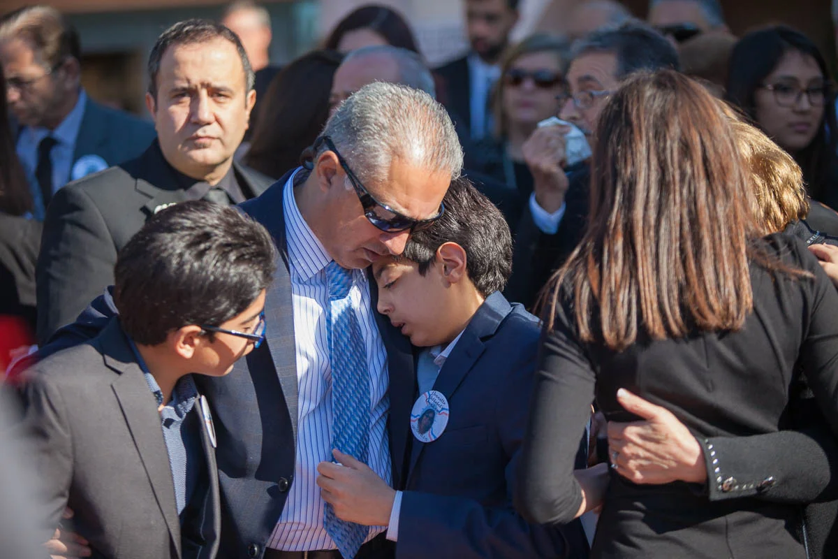 The husband of Bennetta Bet-Badal consoles his two sons as their mother's casket is placed in the hearse at the end of her funeral service at Sacred Heart Church in Rancho Cucamonga, CA