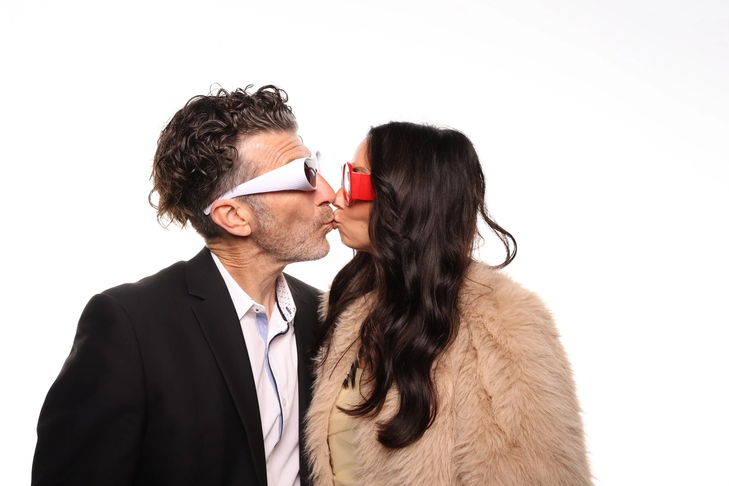 Photo booth pictures of a man and woman are wearing 3D glasses and touching noses while kissing in front of a white background.