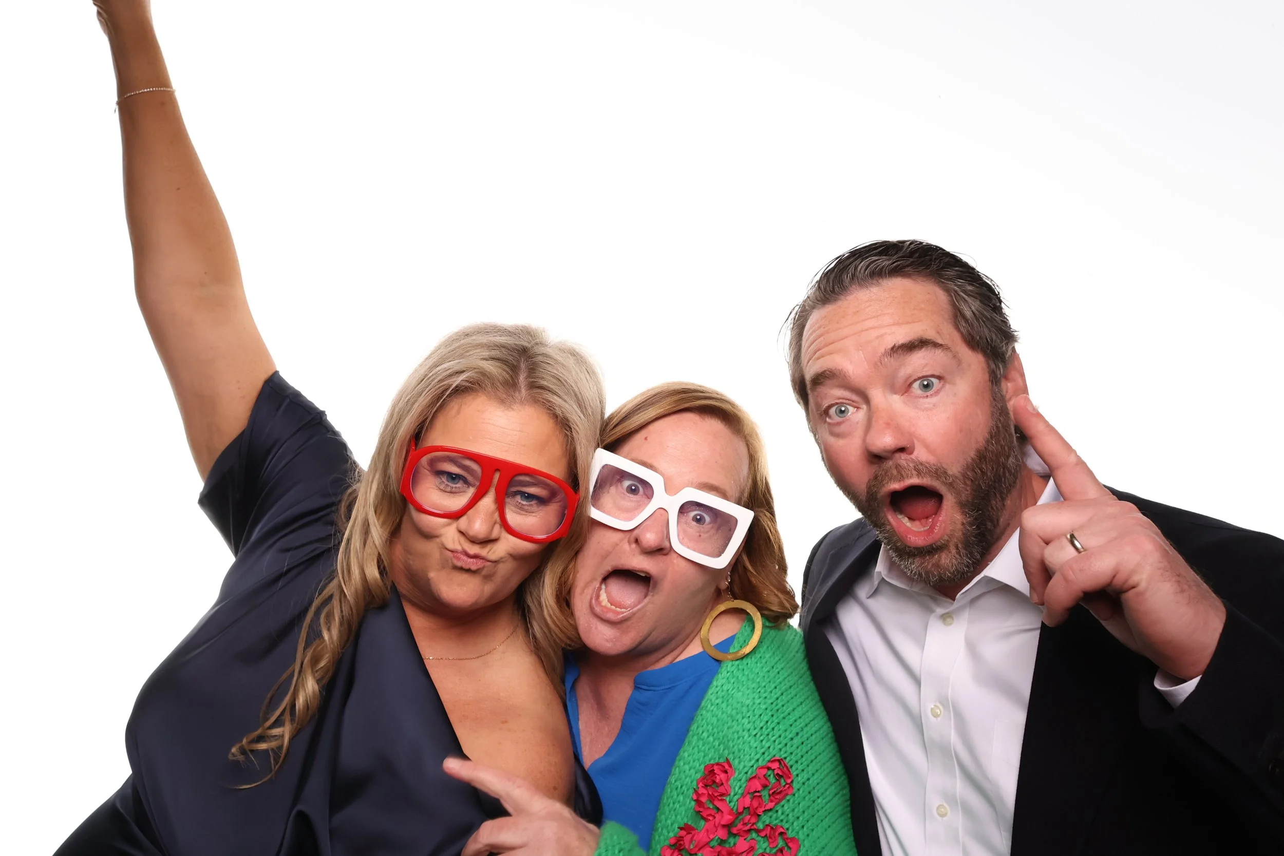 Three adults wearing colorful glasses and accessories, posing with expressive faces against a plain white background.