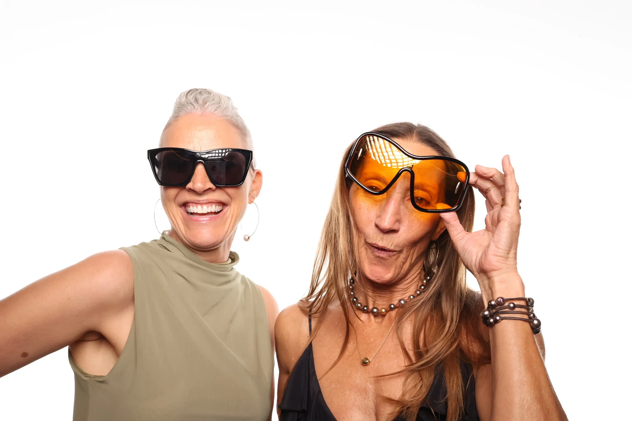Glamorous booth pictures of two women wearing large sunglasses, smiling, and posing for a photo against a plain white background.