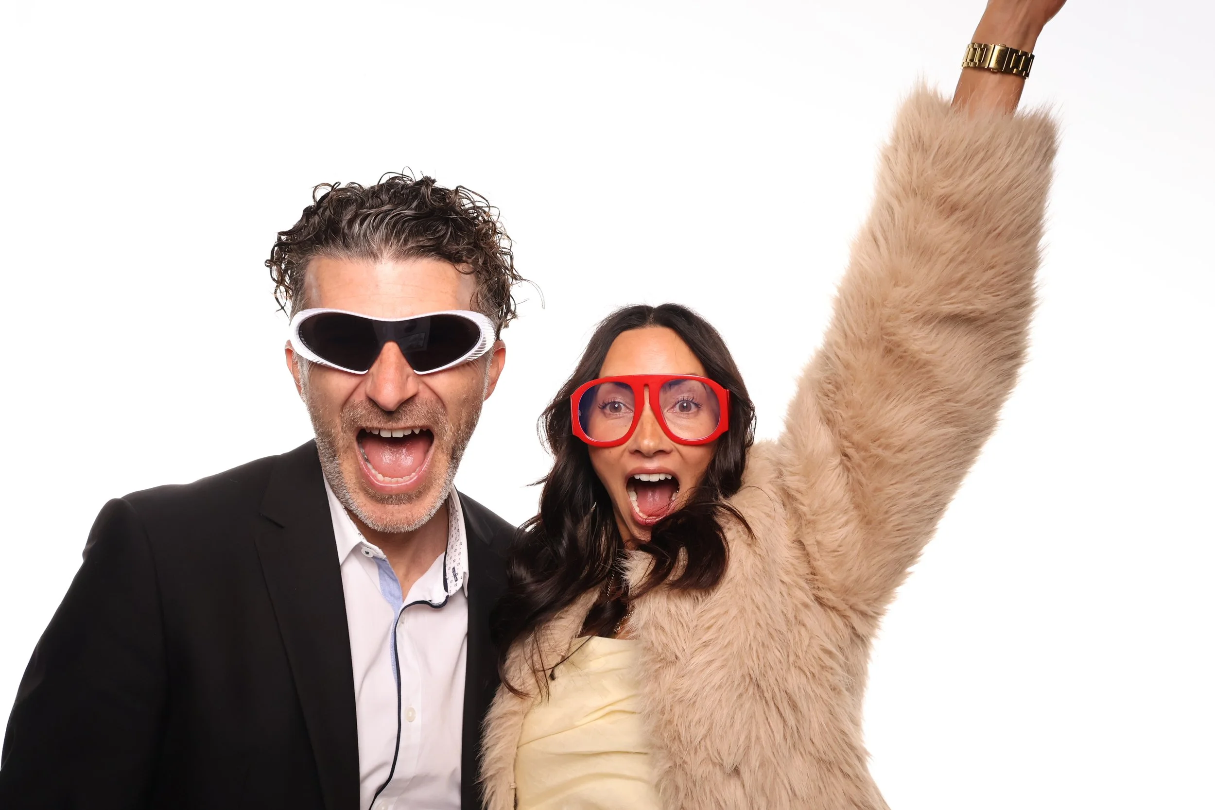 Fun booth pictures of a man in a suit wearing ski goggles and a woman with large red glasses, both expressing excitement, along with a person in a furry costume raising an arm, set against a plain white background.