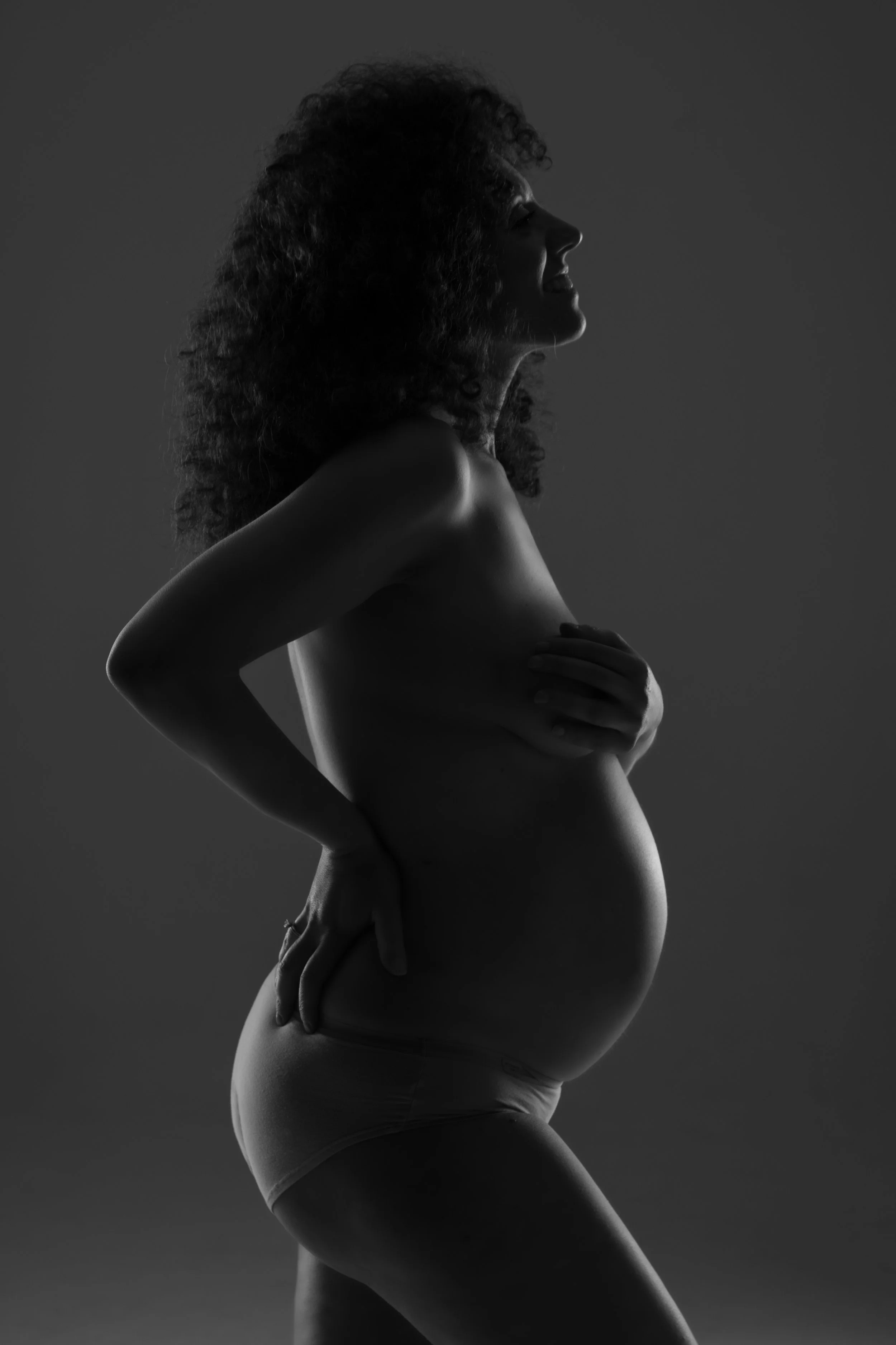 Ritratto fotografico di gravidanza in studio a Milano, in bianco e nero, con futura mamma fotografata di profilo in silhouette.