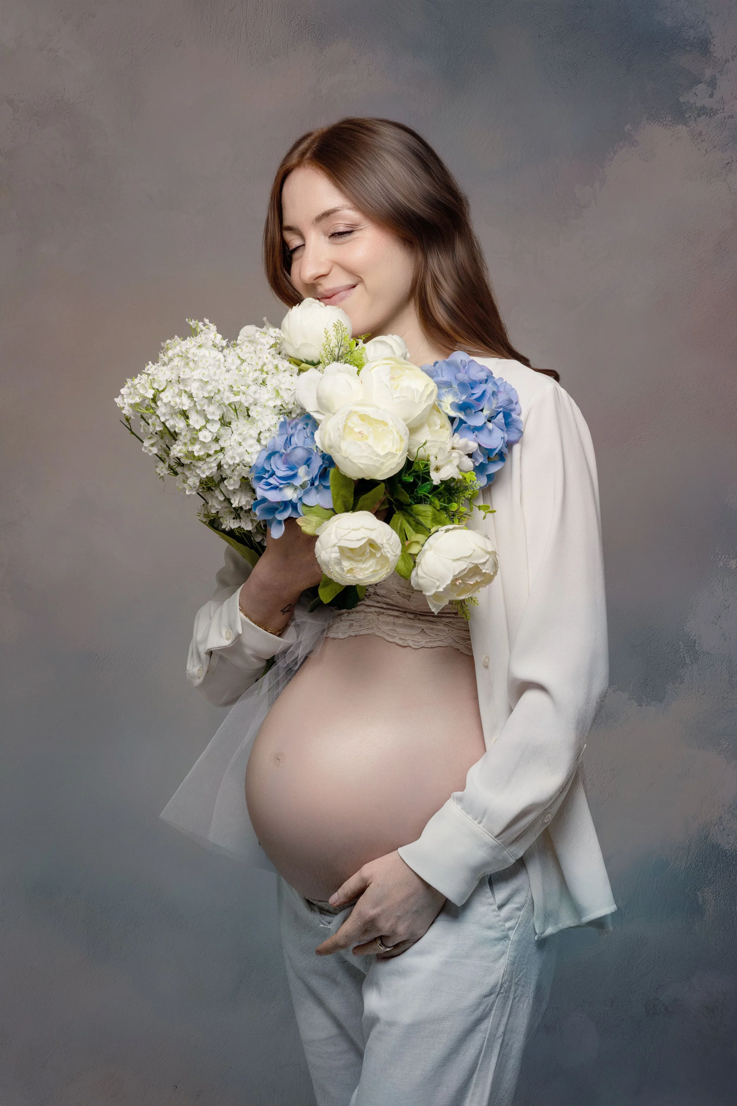 Ritratto fotografico di gravidanza in studio a Milano, con futura mamma e bouquet di fiori bianchi e azzurri.