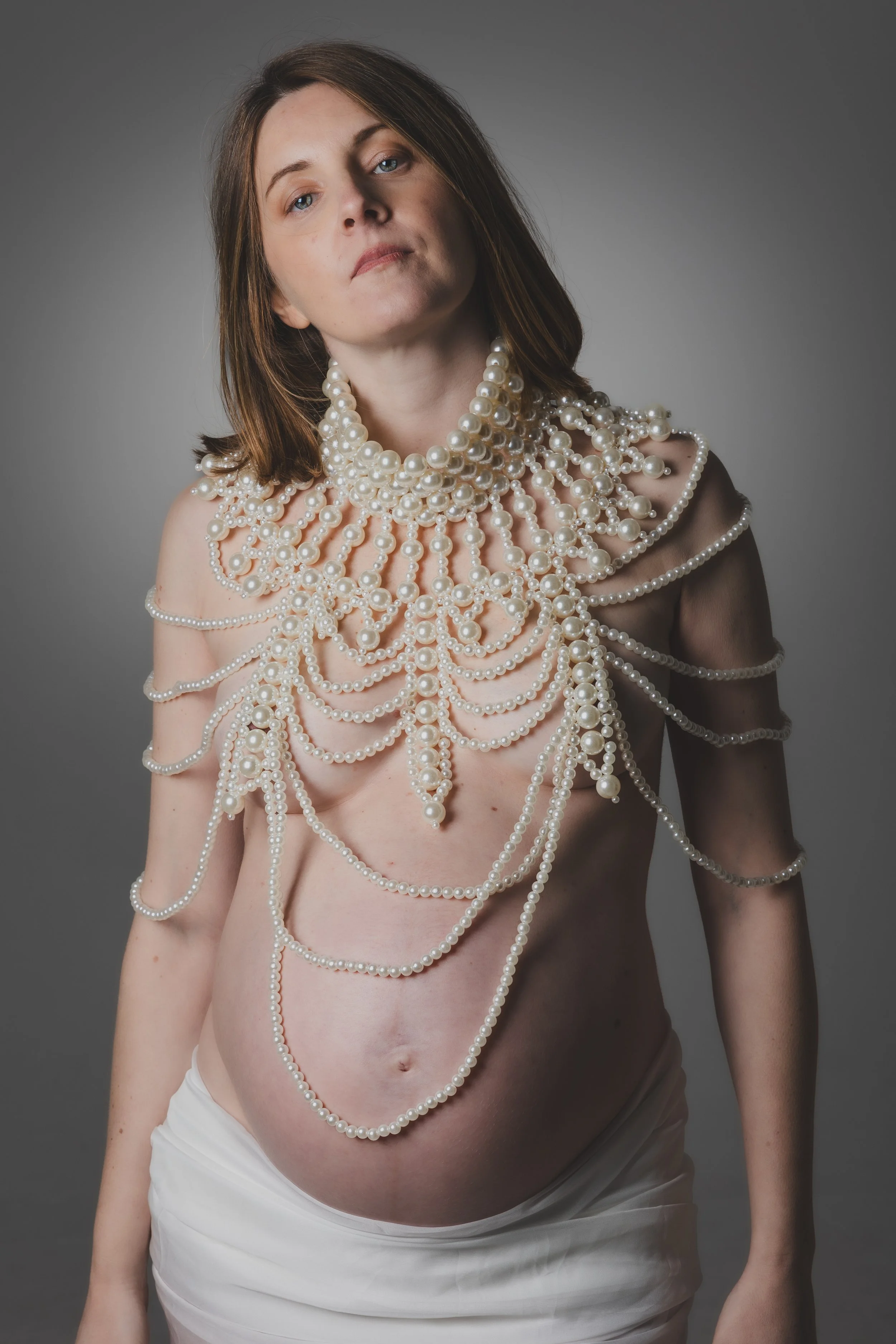 Ritratto fotografico di gravidanza in studio a Milano, con futura mamma avvolta da fili di perle in un’immagine intima ed elegante.