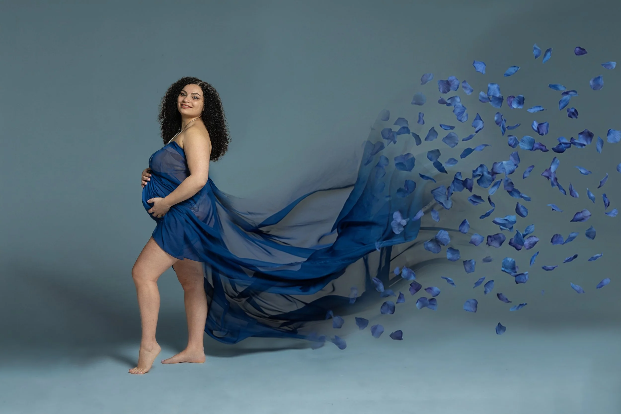 Book fotografico di gravidanza in studio a Milano, con futura mamma avvolta in un velo blu e fiori nei toni dell’azzurro.