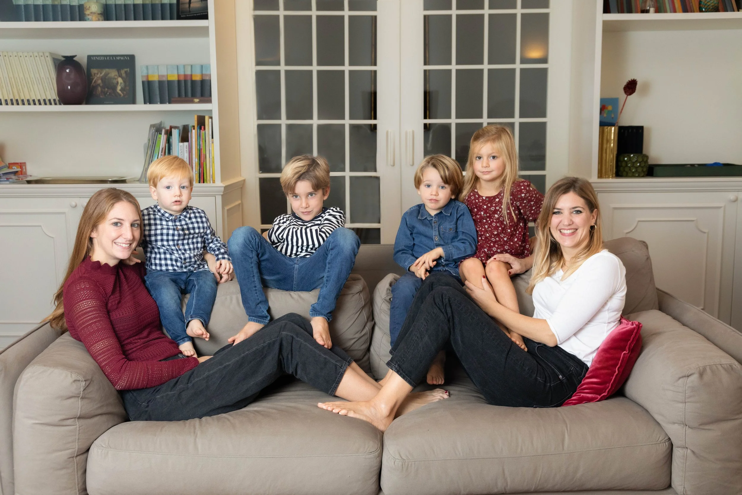 Due mamme con quattro bambini durante un servizio fotografico di famiglia a domicilio nel soggiorno di casa a Milano.
