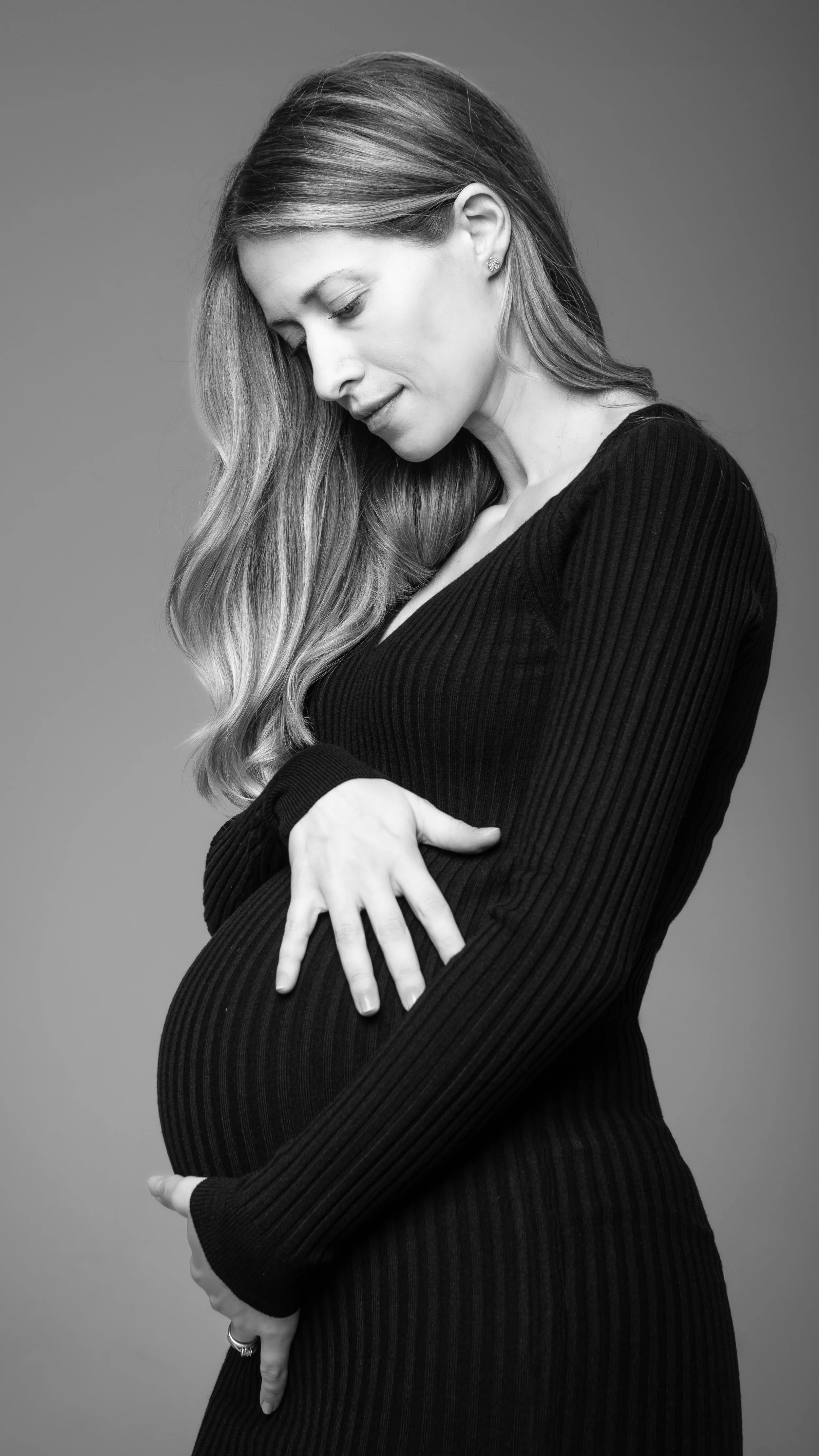 Ritratto fotografico di gravidanza in studio a Milano, in bianco e nero, con futura mamma in abito nero.