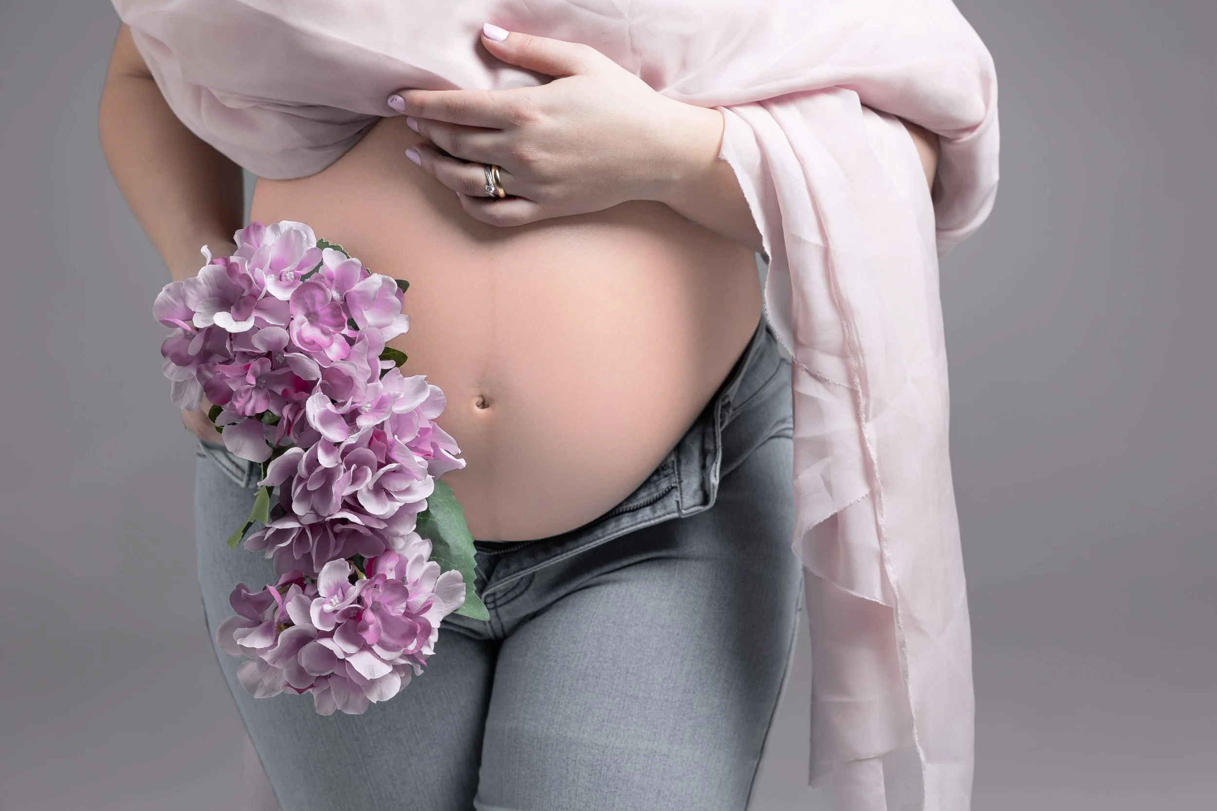 Dettaglio di un ritratto fotografico di gravidanza in studio a Milano, con pancia della futura mamma e fiori rosa.