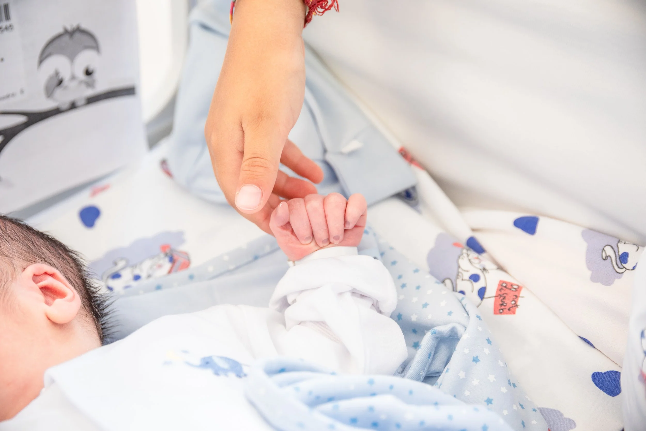 Fotografia di neonato nei primissimi giorni in ospedale, con la mano della mamma che stringe la sua.