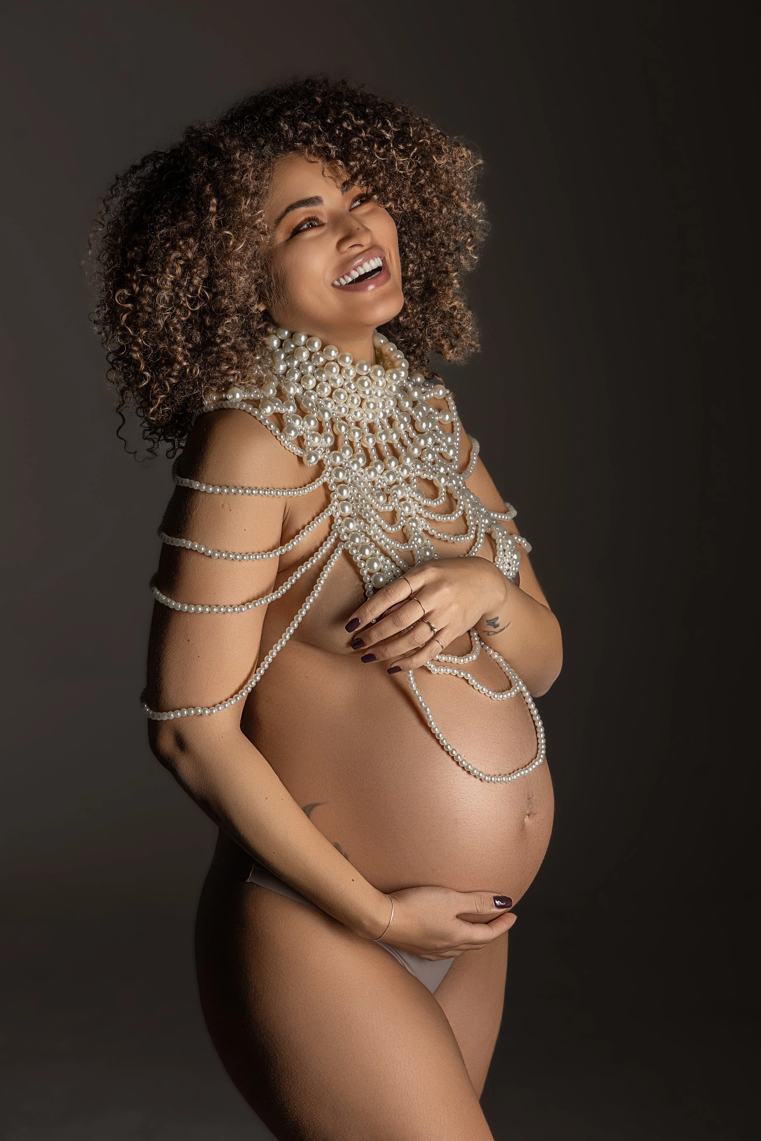 Ritratto fotografico di gravidanza in studio a Milano, con futura mamma alla 38ª settimana avvolta da fili di perle.