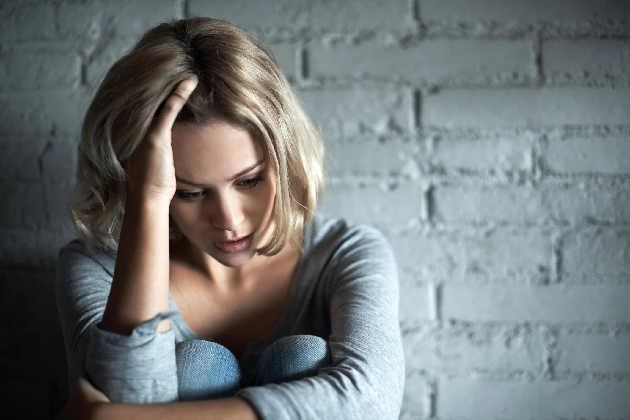 Woman sitting against a wall with hand against her head
