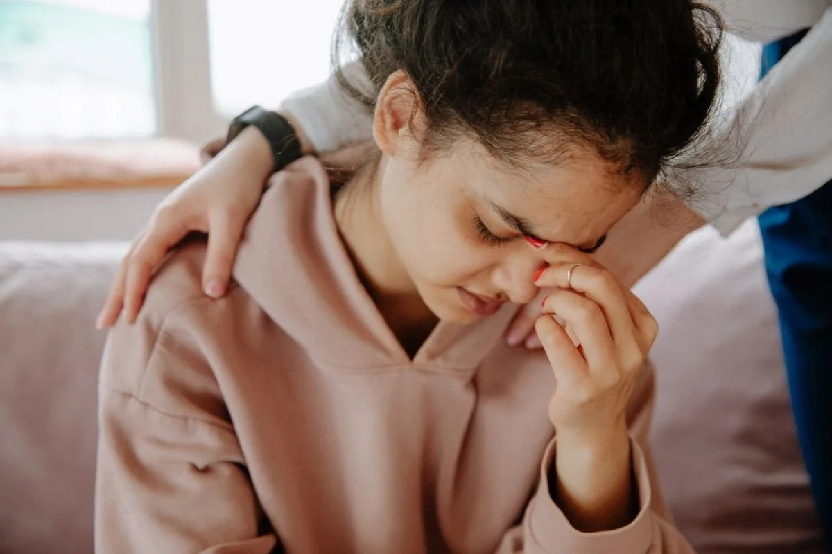 Woman with head down appearing sad with another putting hands on her shoulders