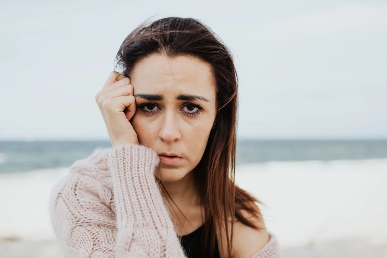 A woman standing looking pensive while standing on the beach