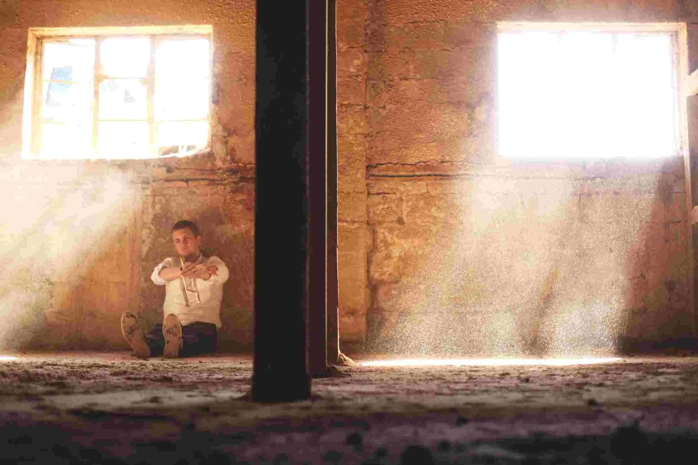 Man sitting on the floor against a wall with a bottle in his hands