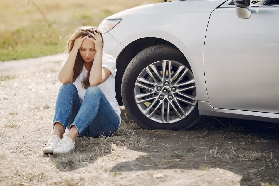 Woman sitting on the side of the road next to car with head in her hands