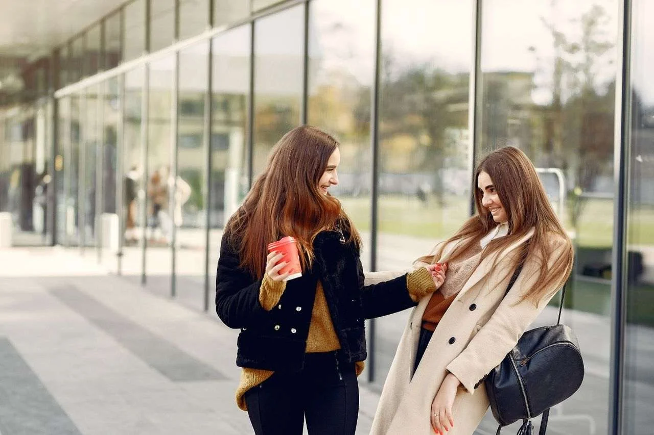 Two young women enjoying a coffee break outdoors, laughing and talking.
