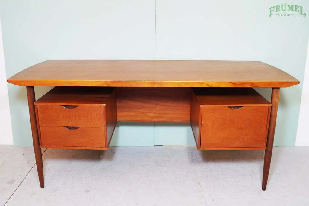 Houten vintage bureau met twee ladeblokken en open opbergruimte, gezet tegen een lichtgroene muur met groene tekst 'FRÜMEL EST 2014' in de rechterbovenhoek.