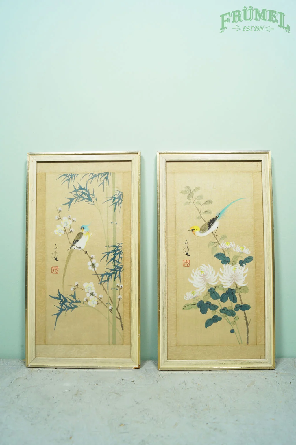 Twee houten schermen met Japanse schilderijen van vogels en bloemen, tegen een lichtblauwe muur met het logo "FRÜMEL" erboven.