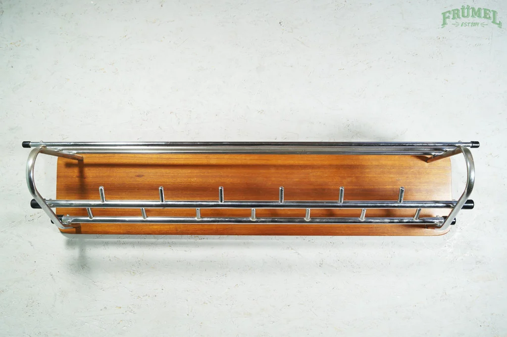 Vintage kapstok met een houten plank en metalen rand, geplaatst op een witte muur met een groene 'FRÜMEL' branding in de hoek.