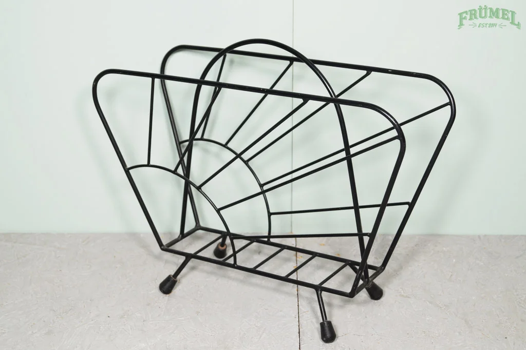 Een lege zwart metalen mand met een spiraalvorm aan de binnenkant, geplaatst op een witte vloer tegen een witte muur.