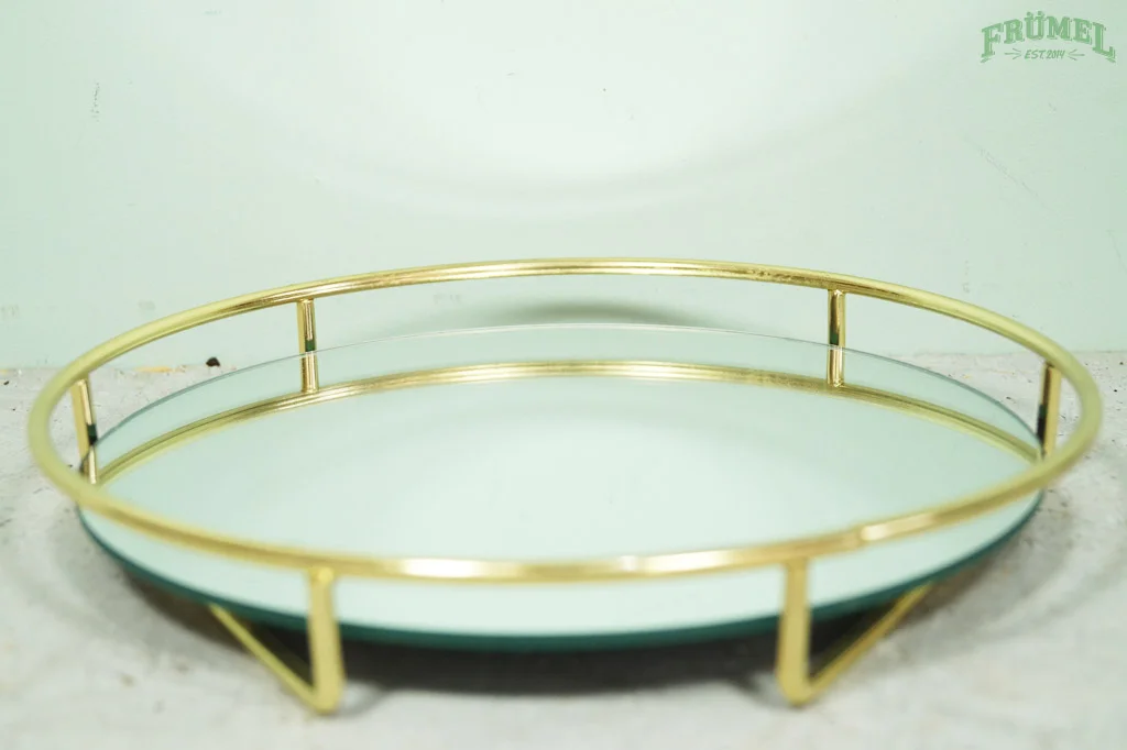 Gouden dienblad met spiegeldriehoek en glazen rand, liggend op een tafel.