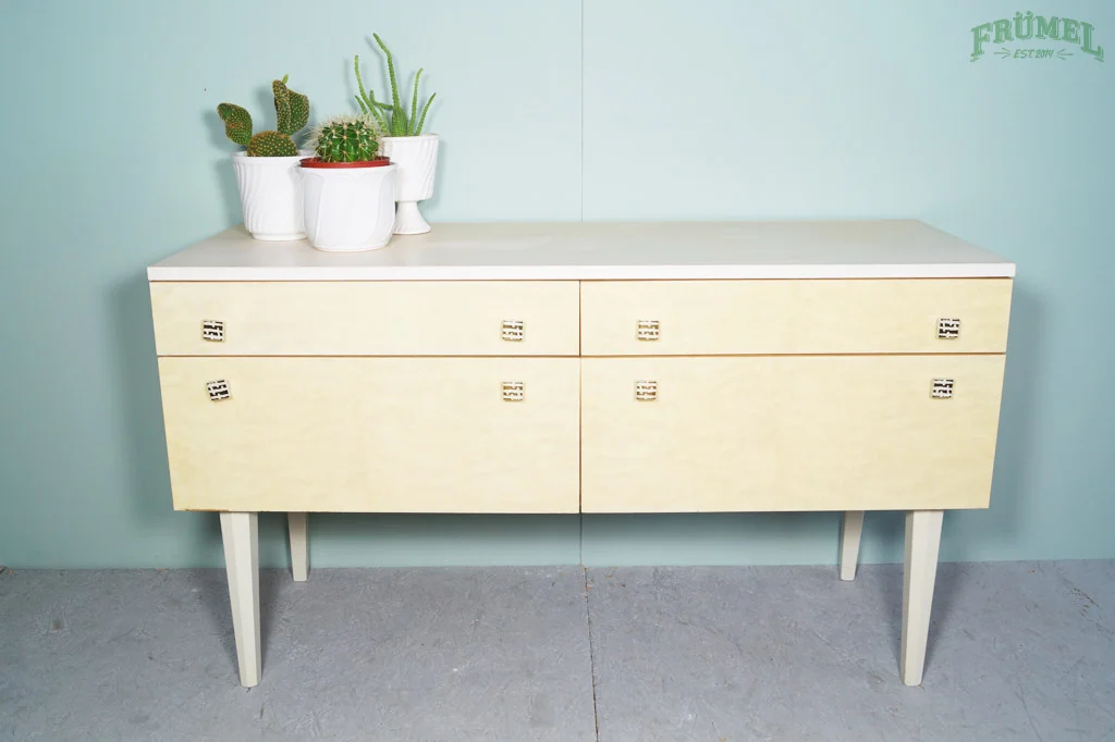 Een witte dressoir met potplanten op de bovenkant, geplaatst tegen een lichtblauwe muur met tekst 'FRÜMEL' in de hoek.