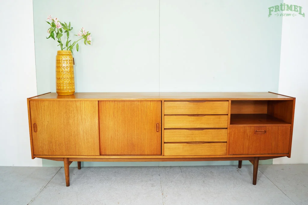 Houten dressoir met zes lades en een open vak, versierd met een gele vaas met roze bloemen, tegen een witte muur.