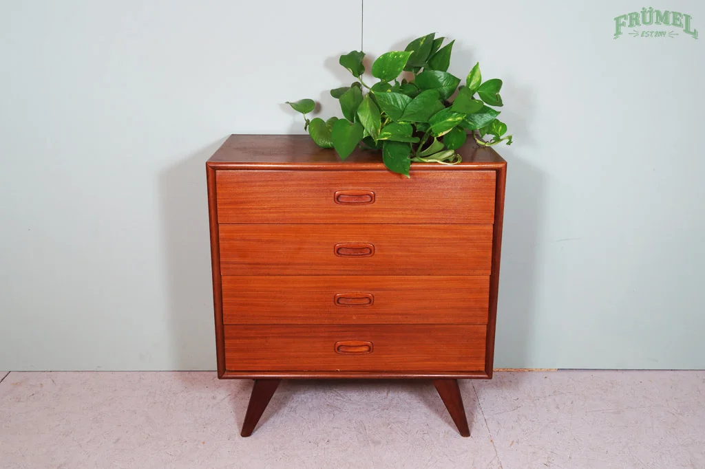 Houten ladekast met vier lades en een groene plant erop, geplaatst tegen een lichtblauwe muur.