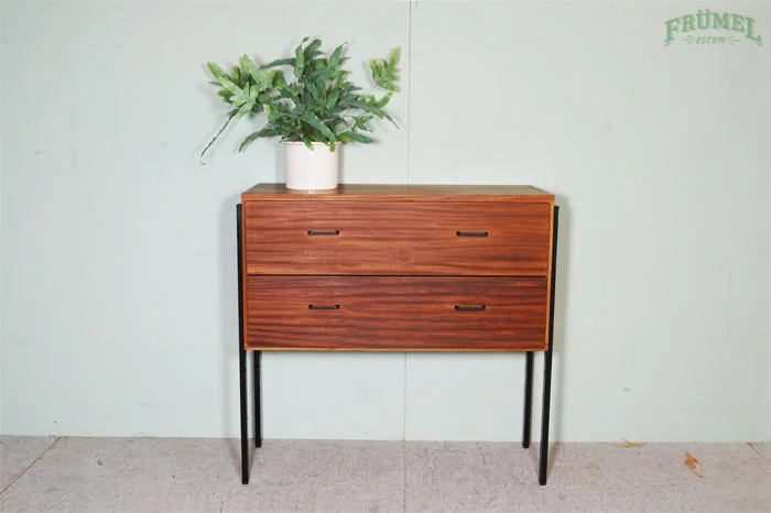 Houten dressoir met vier lades en zwart metalen poten, met een groene plant in een witte pot erop, tegen een lichte muur met de tekst 'FRÜMET' in groen.